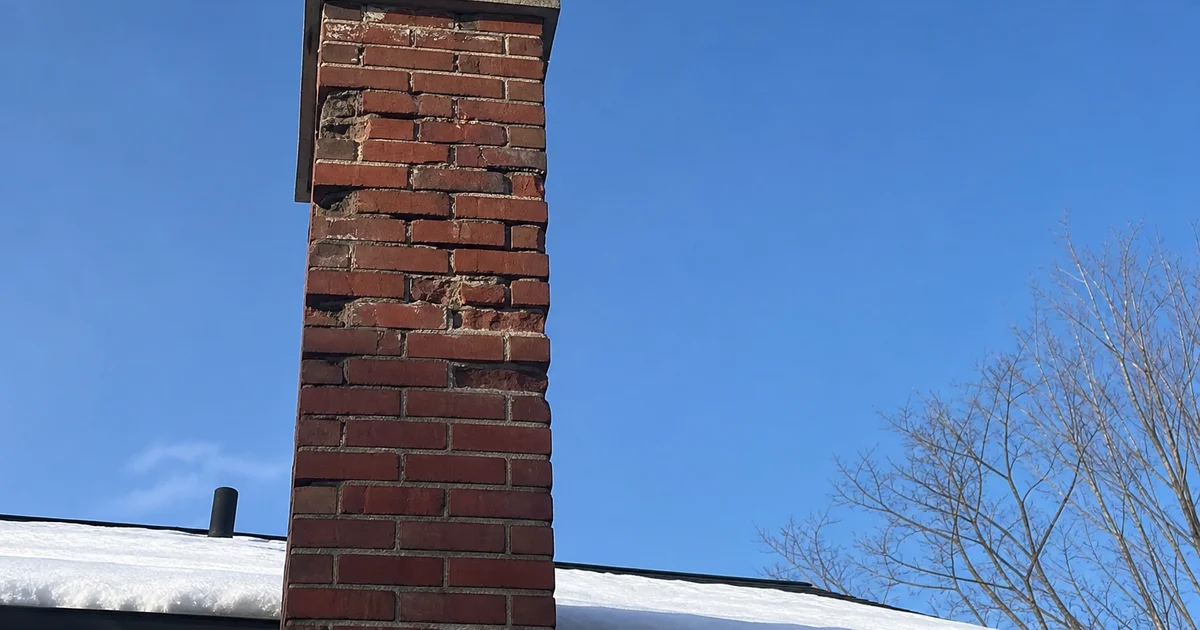 Close-up of a brick chimney with spalling bricks and crumbling mortar