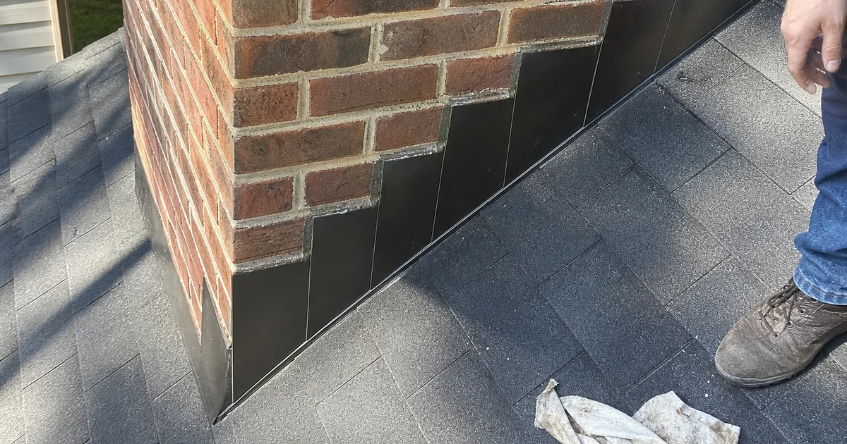 Detail of step flashing where a brick chimney meets the roof shingles