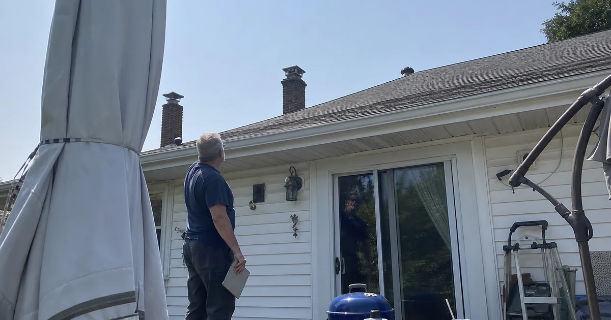Home for sale with a chimney inspector reviewing the roofline