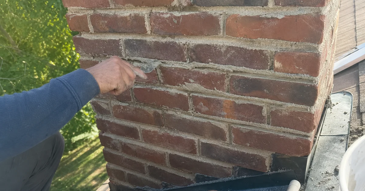 Mason hand-troweling fresh mortar into brick chimney joints