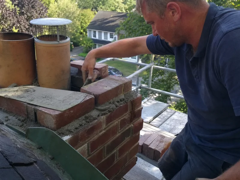 Mason laying new brick during a partial chimney rebuild