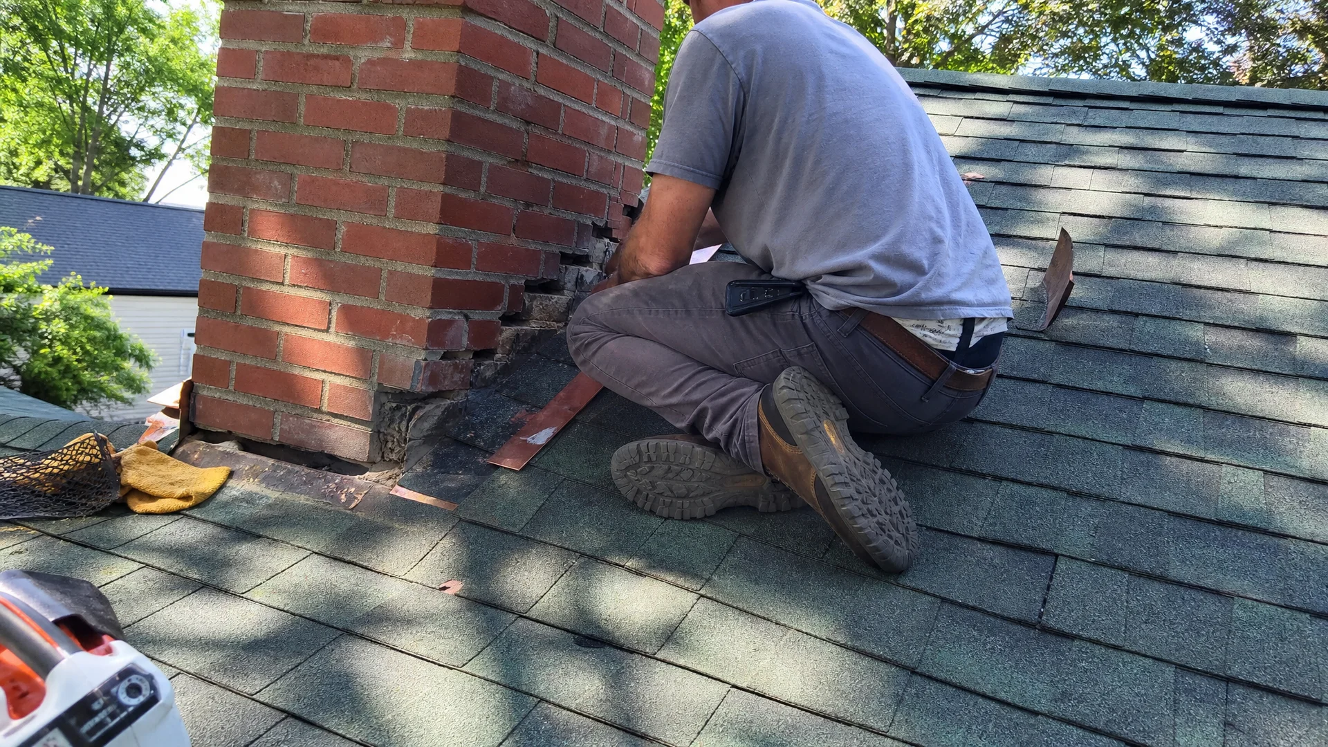 Technician repairing failed step flashing on a chimney at the roofline