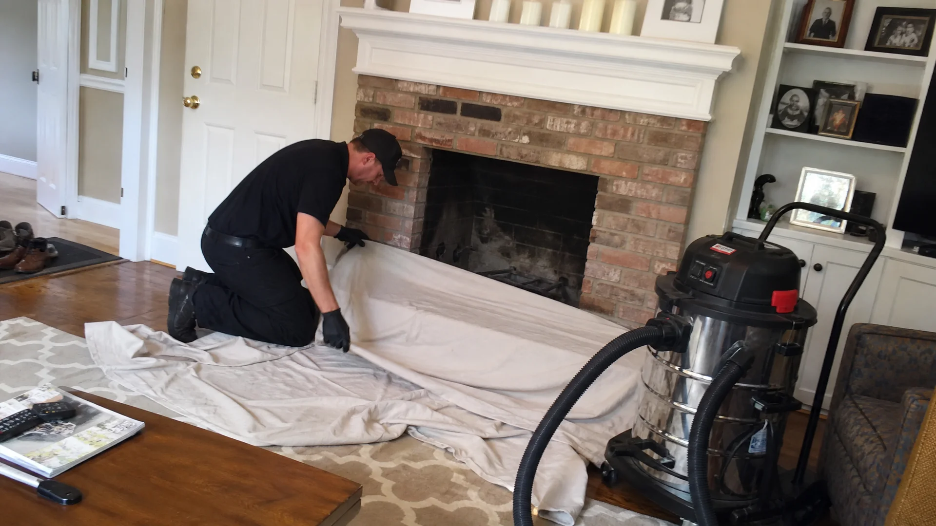 CSIA-certified chimney sweep setting up drop cloths and a HEPA vacuum by a brick fireplace
