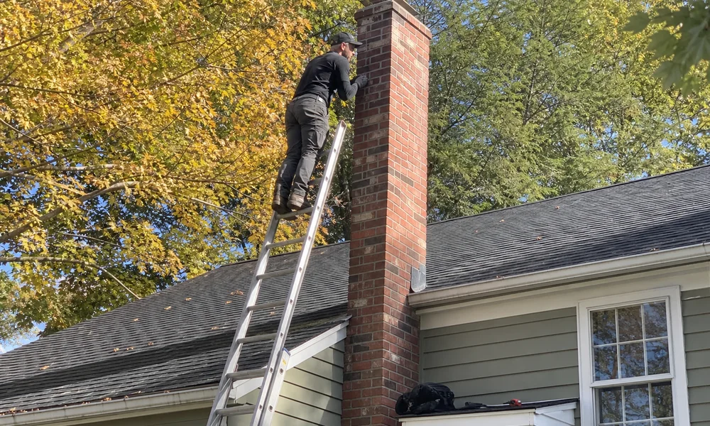 Technician on a ladder inspecting a brick chimney in early autumn