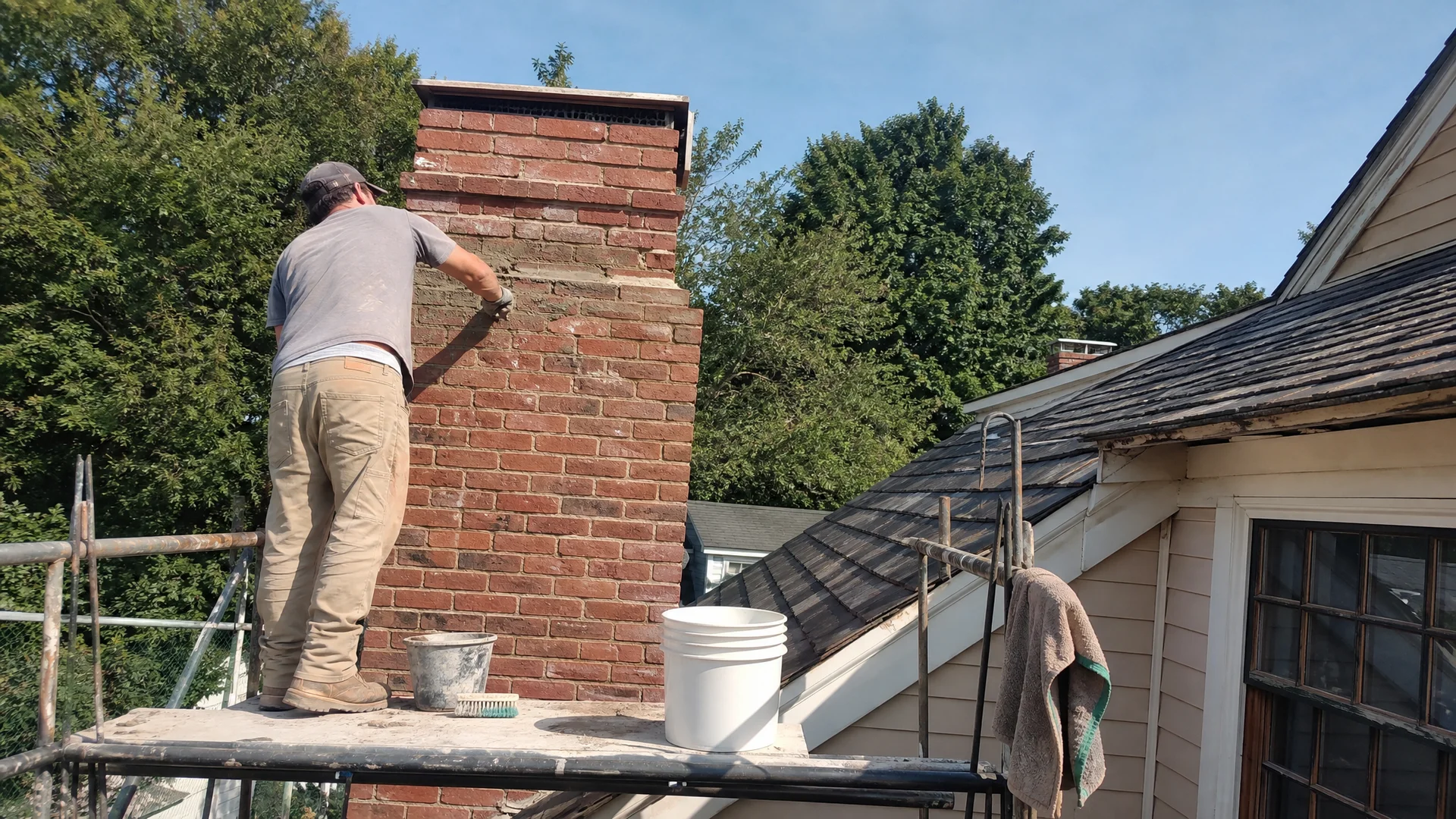 Mason hand-troweling fresh mortar into a brick chimney on a Connecticut home