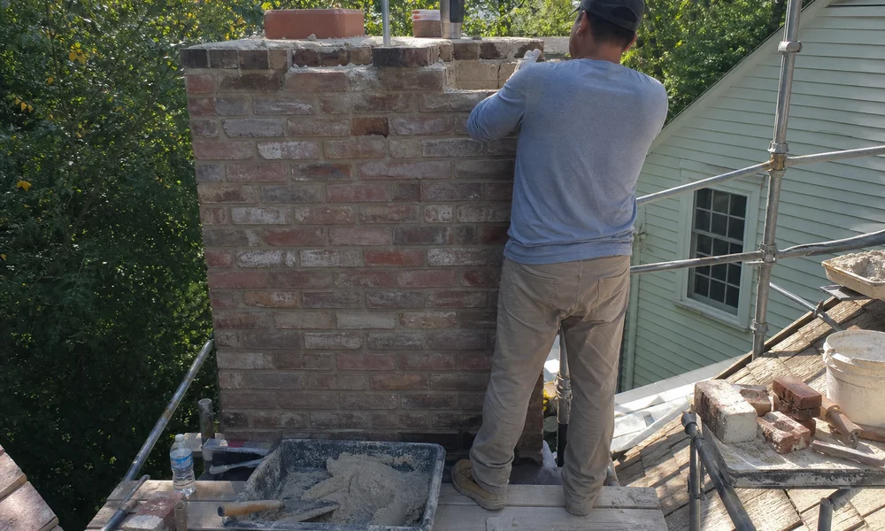 Masonry crew rebuilding a chimney with matched historic brick