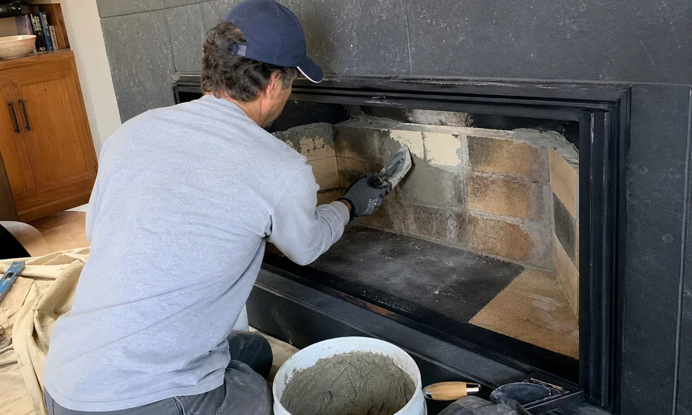 Technician applying refractory mortar to firebricks inside a firebox