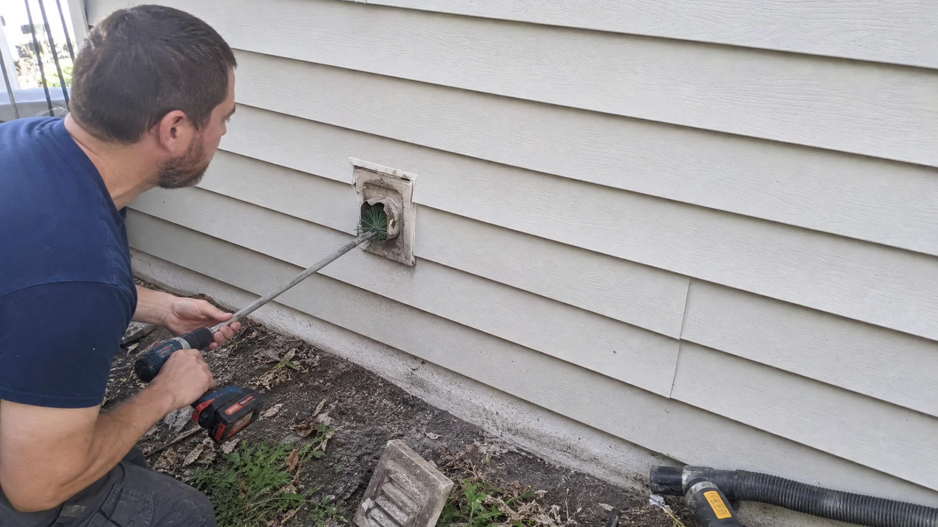 Technician clearing lint from an exterior dryer vent hood