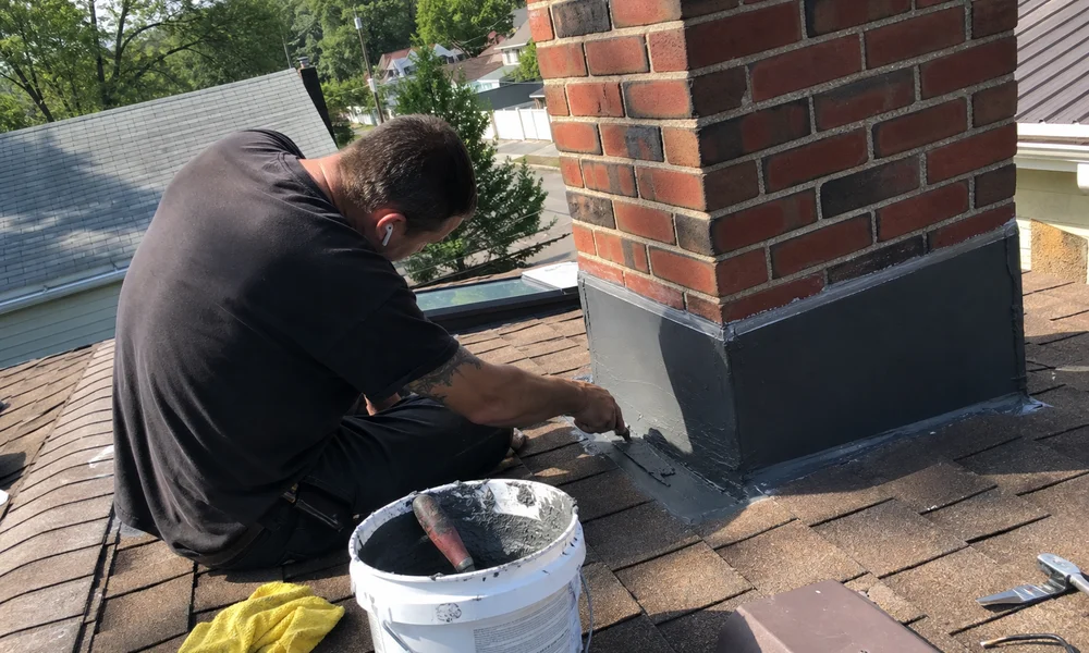 Technician sealing new flashing at a chimney base on a roof